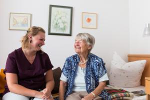 Betreuerin und Seniorin sitzen lachend