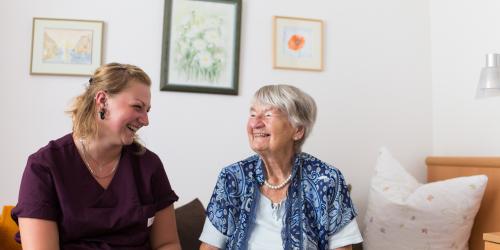 Betreuerin und Seniorin sitzen lachend